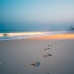 Flick International Serene beach scene at dawn with gentle waves and footprints leading to the water