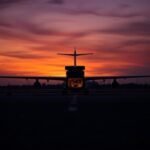 Flick International A dramatic view of an empty airport runway with a parked cargo plane at dusk