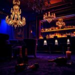 Flick International A dimly lit luxury nightclub scene with plush velvet chairs and a glimmering chandelier