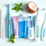 Flick International Flat lay of various oral care essentials including an electric toothbrush, toothpaste, mouthwash, tongue scraper, and water flosser on a bright background