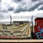 Flick International A stark view of the Delaney Hall ICE detention center in Newark, New Jersey, showcasing heavy gates and barbed wire.