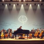 Flick International A serene symphony orchestra stage setup featuring a grand piano and various orchestral instruments symbolizing hope in the fight against Parkinson's disease