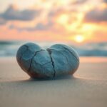 Flick International Close-up of a cracked heart-shaped stone on a beach at sunrise