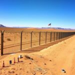 Flick International A rusted metal border fence along the U.S.-Mexico border under a clear blue sky