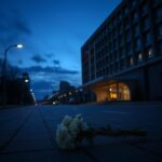 Flick International Exterior view of a modern building resembling an embassy with an abandoned bouquet of white flowers on the pavement