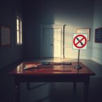 Flick International A somber indoor scene depicting a stark room with a wooden table, an old firearm, and a modern no guns sign.