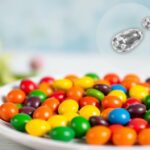 Flick International Close-up of colorful Skittles candies arranged in a vibrant rainbow spectrum on a white plate