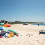 Flick International Colorful beach umbrellas and towels on a sandy beach in Nantucket with distant federal law enforcement presence