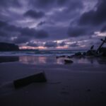 Flick International A dark beach scene at twilight with a broken brick in wet sand