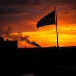 Flick International Dramatic sunset over a cityscape with silhouettes of urban buildings, reflecting tension and unrest