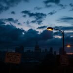 Flick International Dramatic urban landscape at dusk with a silhouette of a city skyline and a broken street sign