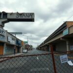 Flick International Somber urban landscape in Los Angeles with boarded-up storefronts and graffiti about immigration