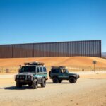 Flick International Secure U.S.-Mexico border wall with patrol vehicles under a clear blue sky