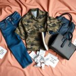 Flick International Close-up of a flat lay featuring unchic fashion items including baggy jeans, a camouflage shirt, worn athletic shoes, and a luxury handbag.